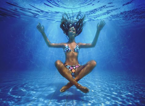 Underwater shoot of a relaxed smiling woman flying in a swimming pool in lotus position