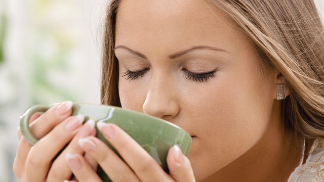 Closeup portrait of beautiful girl drinking tea from green cup.