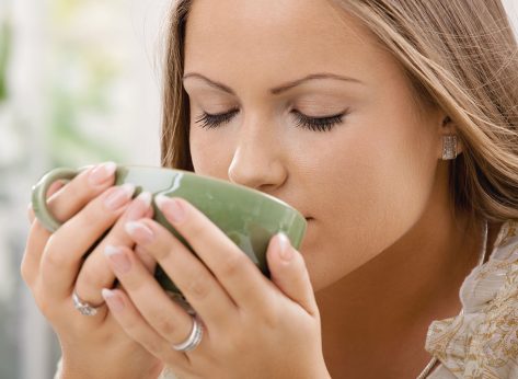 Closeup portrait of beautiful girl drinking tea from green cup.