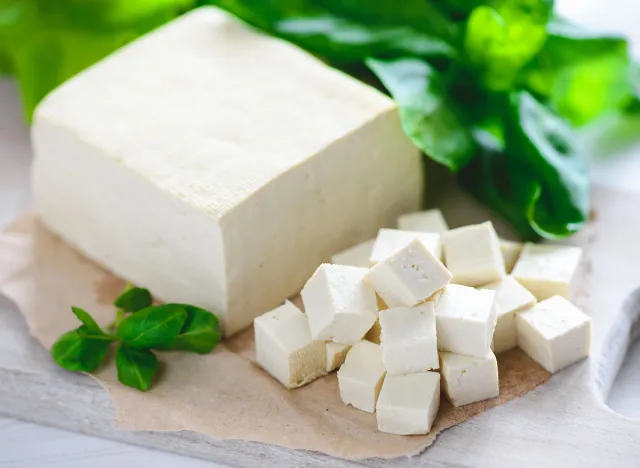 soy cheese tofu diced on a cutting board, basil closeup