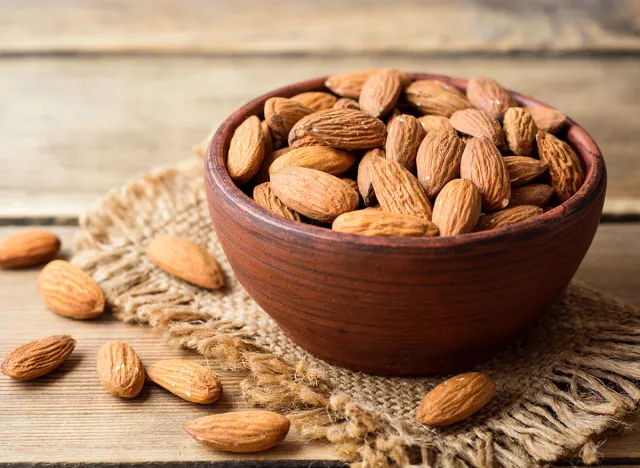 Almonds in ceramic bowl on wooden background. Selective focus.