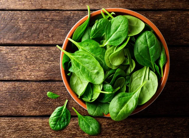 Fresh spinach leaves in bowl on rustic wooden table. Top view.