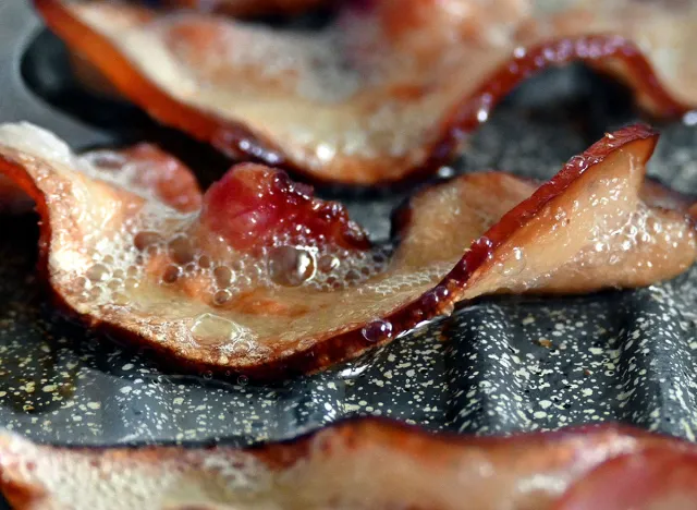 A banner for a cooking site with bacon slices fried in oil with bubbles in a grill pan close-up.