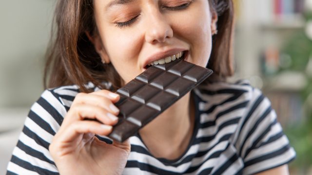 Young,Woman,Eating,Chocolate,Bar,In,Living,Room
