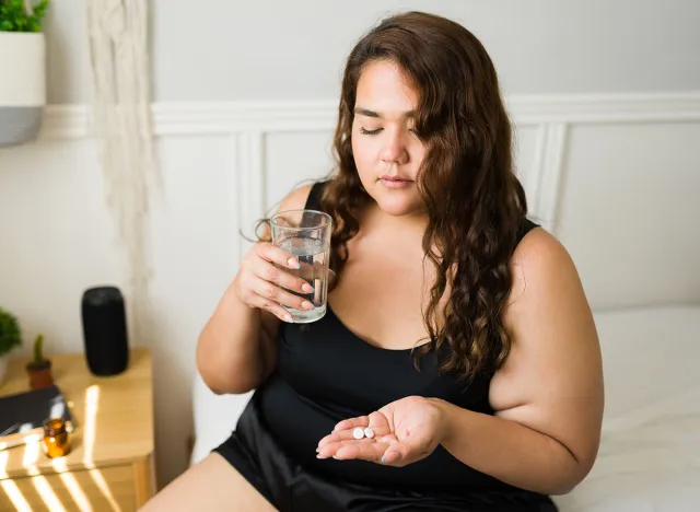 Healthy obese woman taking vitamins to feel better during the morning. Sick woman taking pills in bed