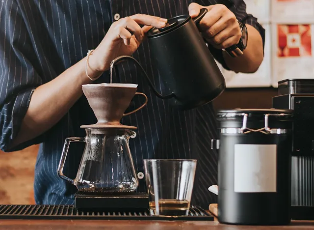 Professional barista making filtered drip coffee in coffee shop. Close up of hands barista brewing a drip hot espresso, pour over coffee with hot water and filter paper in cafe.