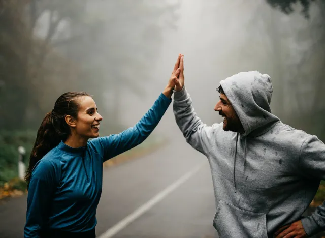 Two people in sports outfits have an active HIIT workout in the forest. Woman and a man giving each other a high five after a outdoor workout