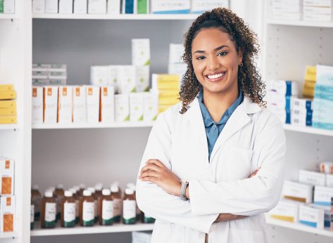 Pharmacy, pharmacist or portrait of woman with arms crossed or smile in customer services or clinic. Healthcare help desk, wellness or happy doctor smiling by medication on shelf in drugstore