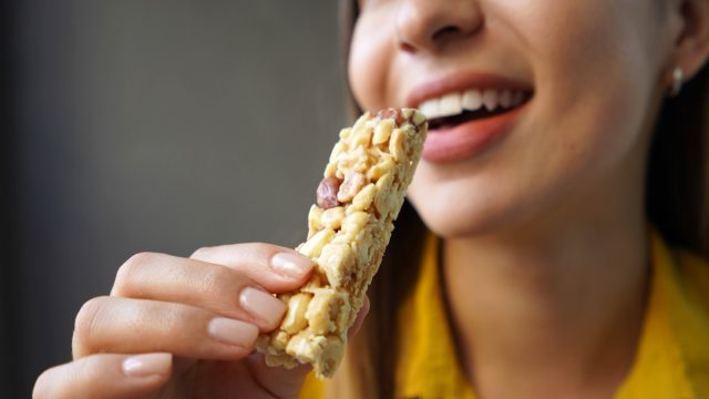 Young,Woman,Eating,A,Nuts,Cereal,Bar,Without,Sugar,On