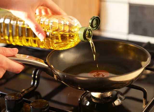 Vegetable fats. Woman pouring oil into frying pan on stove, closeup