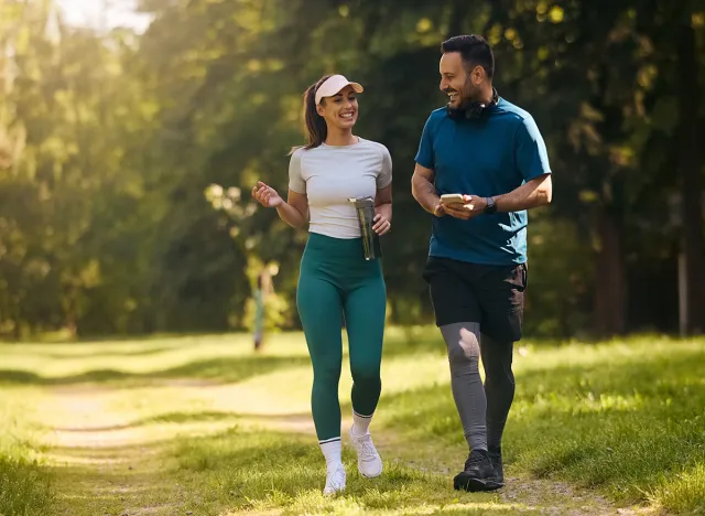 Happy athletic couple communicating while walking in nature after sports training. Copy space.