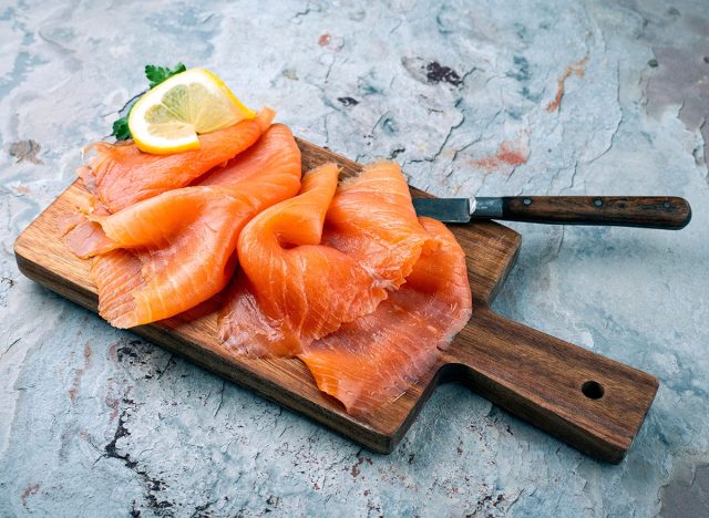 Traditional Norwegian smoked salmon in slices with parsley and lemon served as close-up on rustic wooden chopping board with text space