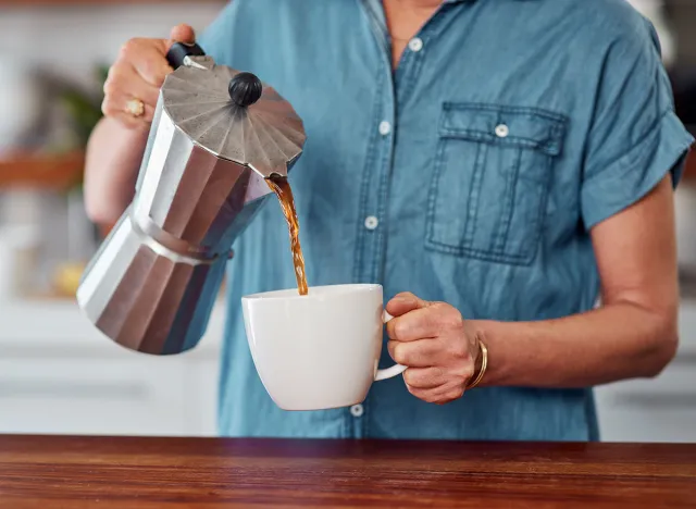 Woman, hands and coffee with moka pot for morning, caffeine or breakfast beverage in mug at home. Closeup of female person pouring latte, cappuccino or espresso for drink, energy or liquid in kitchen