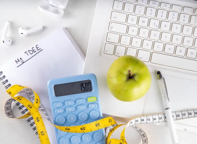 Calorie calculator, healthy TDEE concept. Calorie calculation based on total daily energy expenditure, background with calculator, notebook, measuring tape, apple. Healthy weight loss diet background