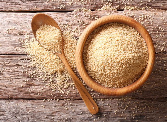 Raw Couscous in a wooden bowl and spoon on the table. Horizontal top view