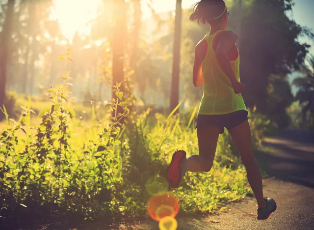 Young fitness woman running at morning tropical forest trail