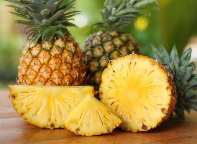 Close up,Sliced and half of Pineapple(Ananas comosus) on wooden table with blurred garden background.Sweet,sour and juicy taste.Have a lot of fiber,vitamins C and minerals.Fruits or healthcare concept