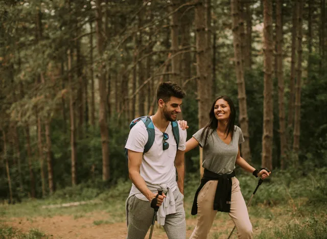 Couple of young hikers with backpacks walk through the forest