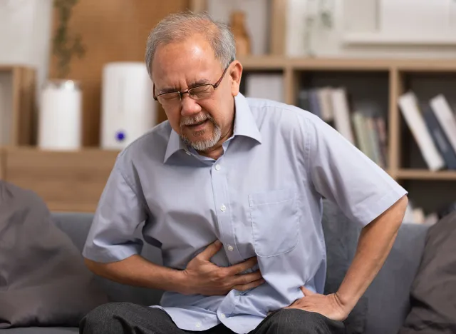 Senior men holding his stomach feeling pain while sitting on the sofa at home. Asian man having stomachache with isolated gastric. Senior suffering from digestion problem or acid reflux.