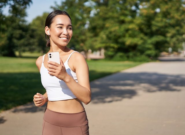 Happy smiling asian woman jogging in park. Healthy young female runner doing workout outdoors, running on streets.