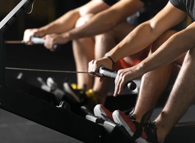 Two young male athletes doing rowing practice at dark concept gym.