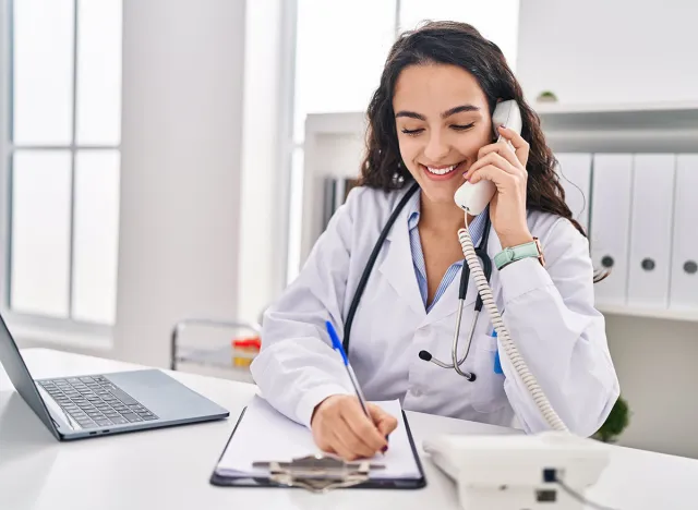 Young hispanic woman wearing doctor uniform talking on the telephone at clinic