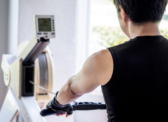 Active Asian athlete man pulling bar doing exercise on rowing machine in fitness gym. Indoor physical training and muscular building concepts