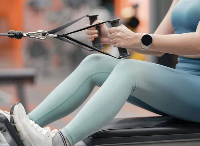 Young woman training on row machine weight training equipment on sport gym.