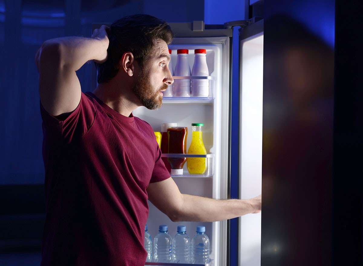 A hungry man choosing food from refrigerator in kitchen at night. Bad habit