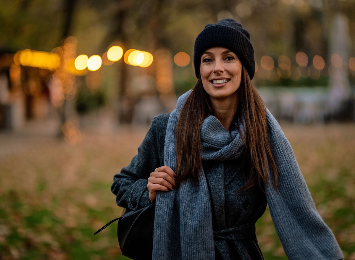 Beautiful mid aged woman walking at city park in an autumn day. Smiling female wearing coat and beanie.
