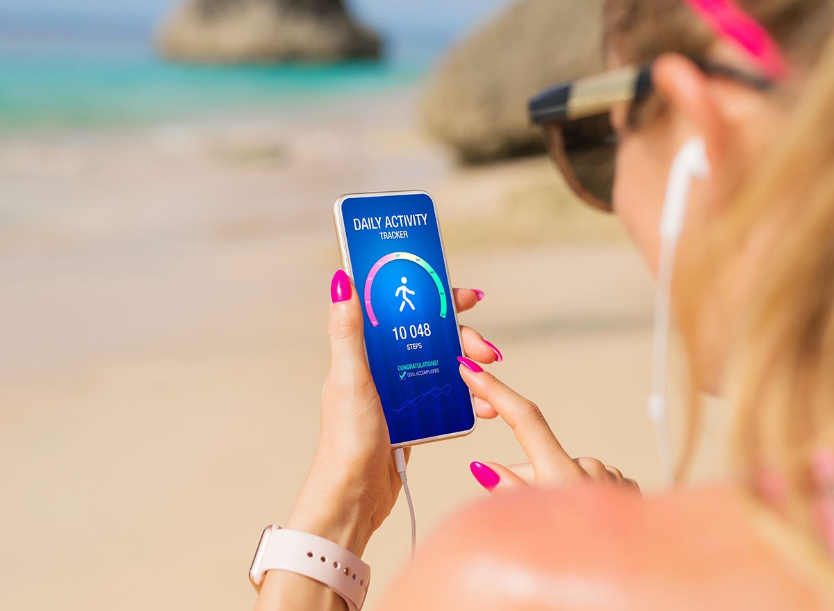Woman using daily activity tracking app on mobile phone showing 10 000 steps daily goal achievement