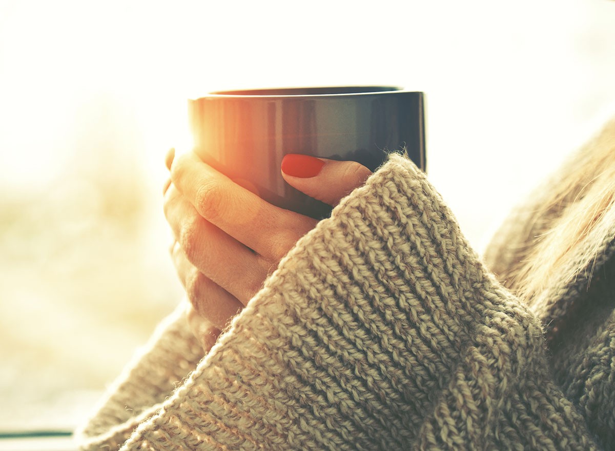 hands holding hot cup of coffee or tea in morning sunlight