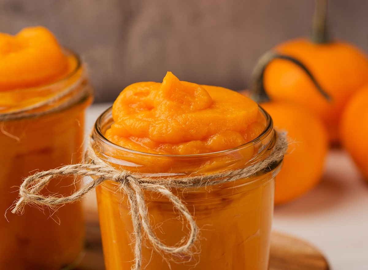 Homemade organic pumpkin puree in glass jars and mini pumpkins on dark background close up. Ingredient for autumn or winter recipes. Seasonal cooking concept. Fall time. Macro with shallow dof.