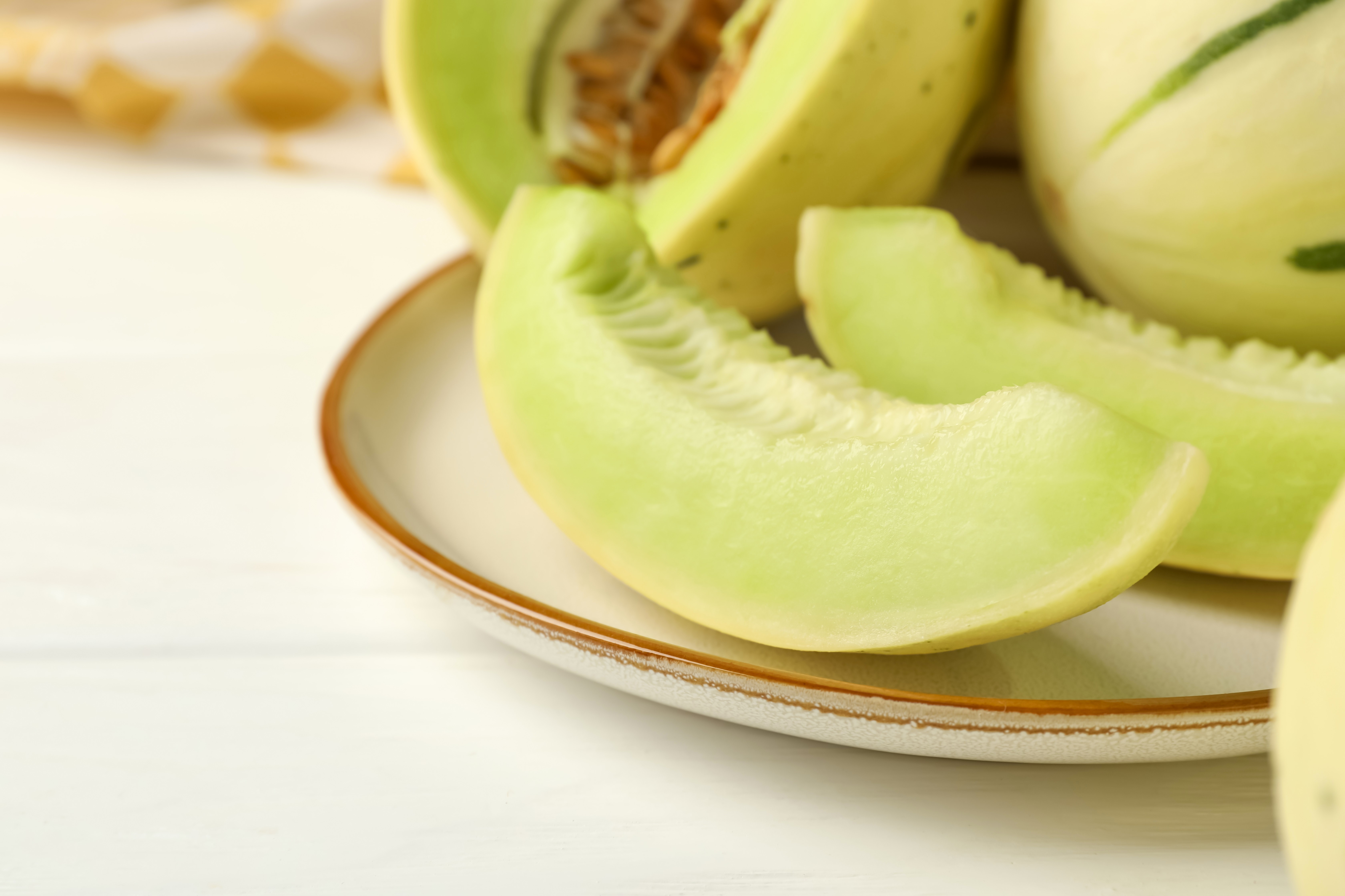 Fresh whole and cut honeydew melons on white wooden table, closeup