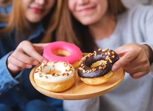 Closeup image of a young couple women holding and eating donuts together