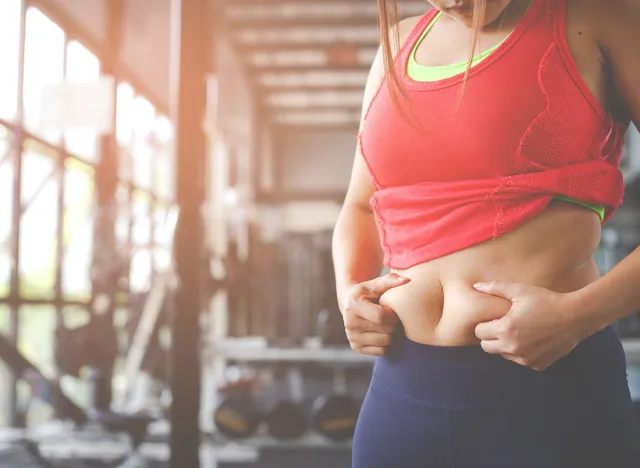 Fat woman, Obese woman hand holding excessive belly fat isolated on gym background, Overweight fatty belly of woman, Woman diet lifestyle concept to reduce belly and shape up healthy stomach muscle.