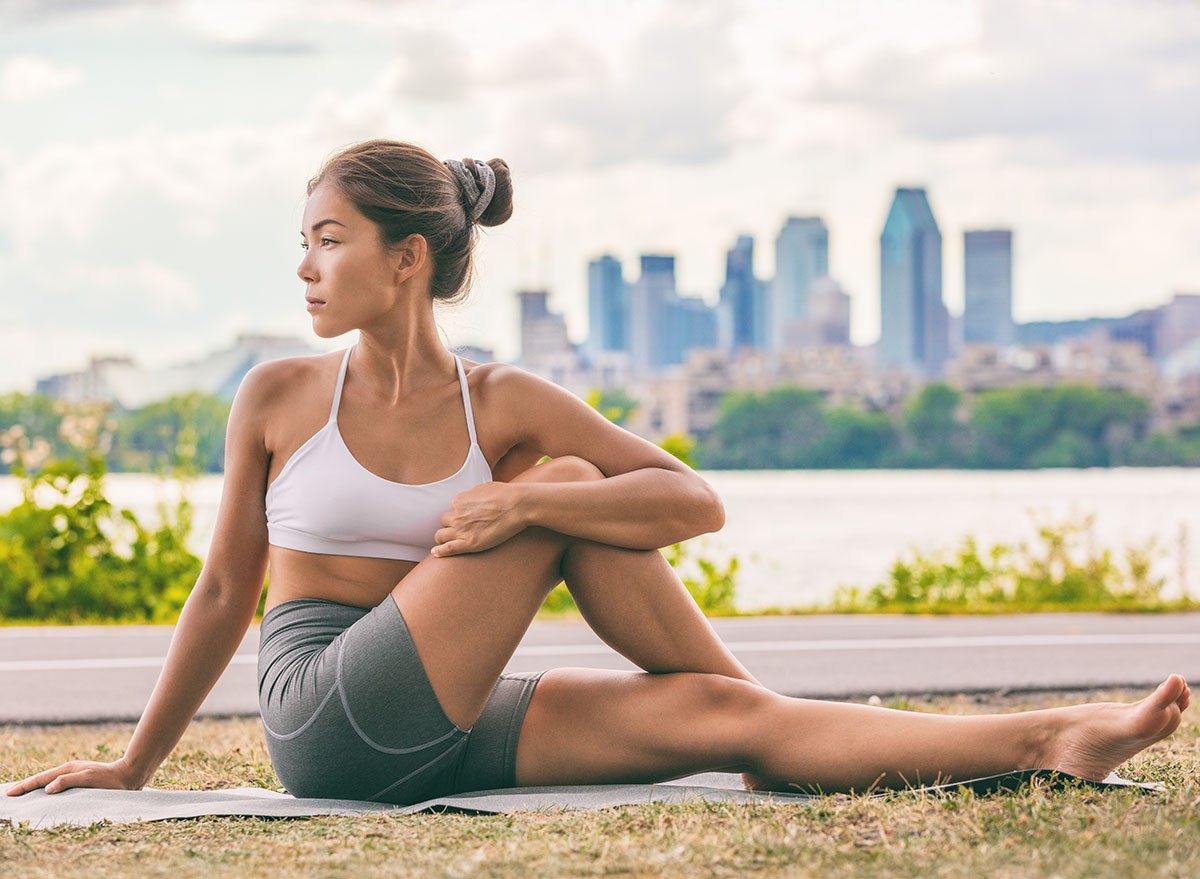 Yoga stretch exercise fit Asian woman stretching lower back for spine health on city outdoor fitness class in park. Seated spinal twist.