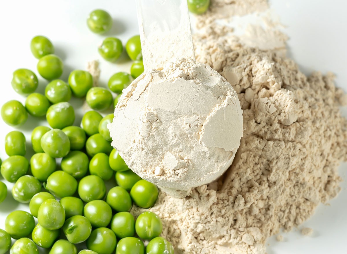 Plant base protein Pea Protein Powder in plastic scoop with fresh green Peas seeds on white Background, isolated copy space.