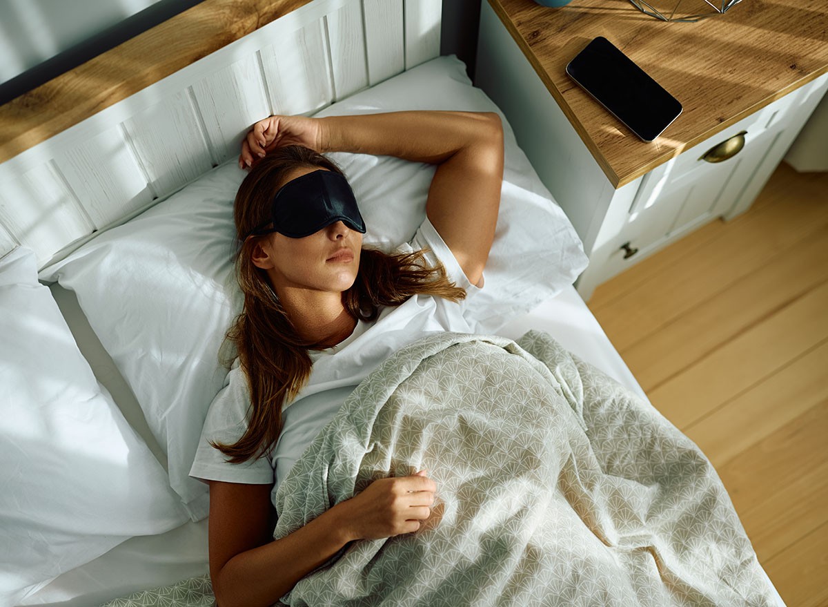 High angle view of woman wearing sleeping eye mask in bed.