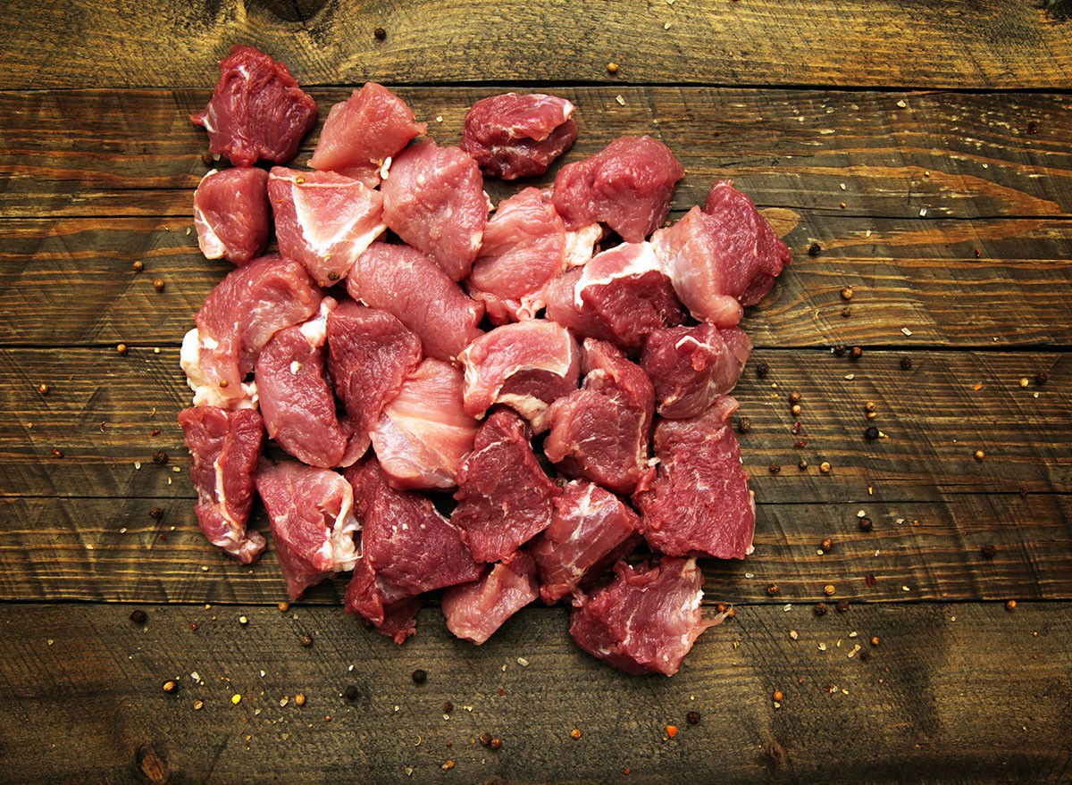 Creatively lit, a fresh raw cube of diced red beef meat prepared for cooking, shot against a dark rustic background with placement to copy the space.