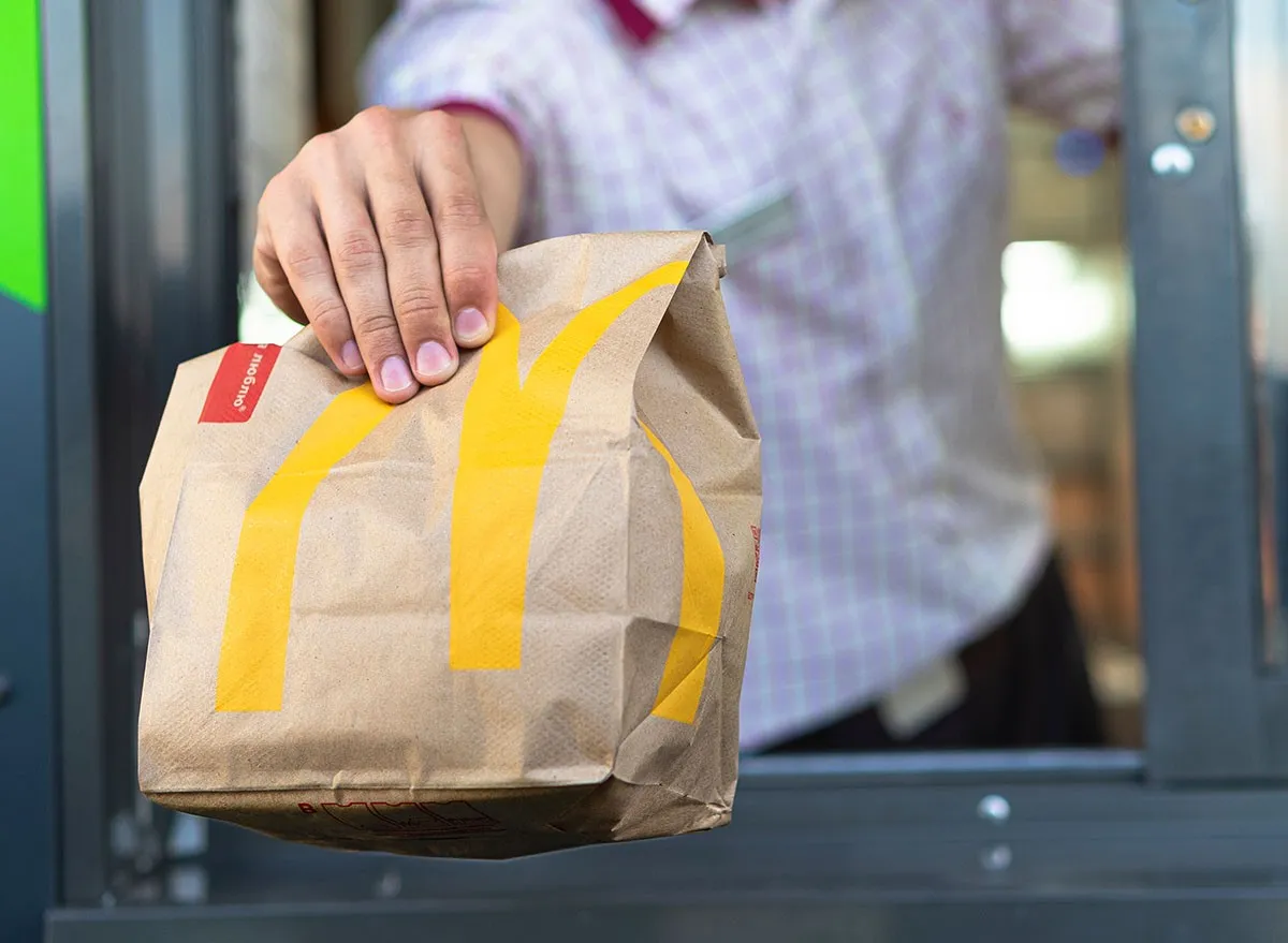 McDonalds worker holding bag of fast food. Hand with a paper bag through the window of mcdonalds car drive thru service.