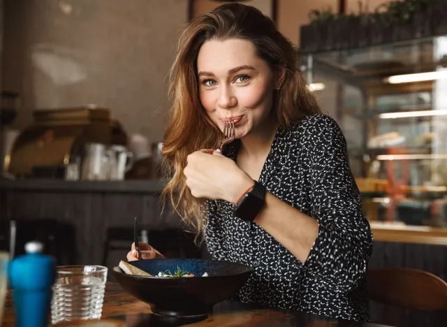 Photo of excited beautiful young pretty woman sitting in cafe indoors have a breakfast eating salad
