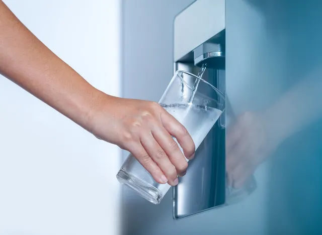 Water dispenser from dispenser of home fridge, Woman is filling a glass with water from the refrigerator.