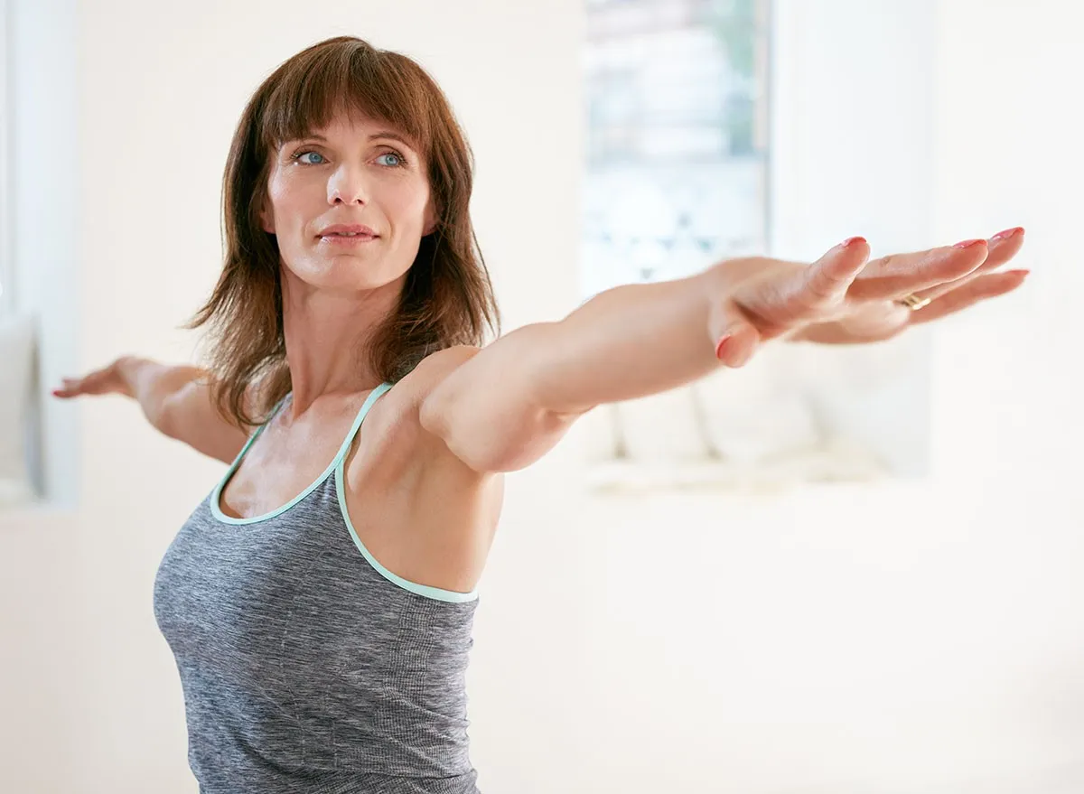 Portrait of mature woman stretching her arms and looking away at gym. Beautiful woman performing yoga in warrior pose, Virabhadrasana.