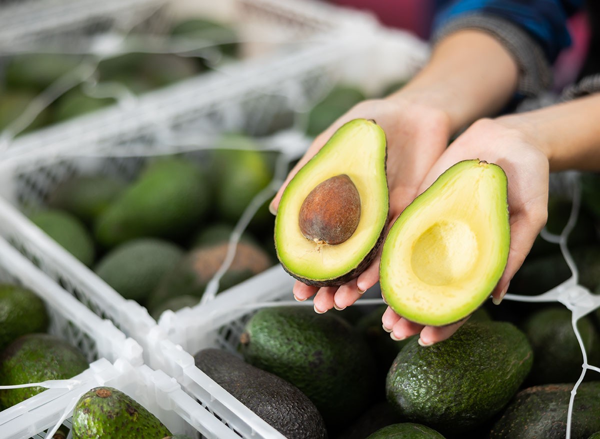 Close-up of two halves of ripe hass avocado in hands of female fruit sorting factory worker..