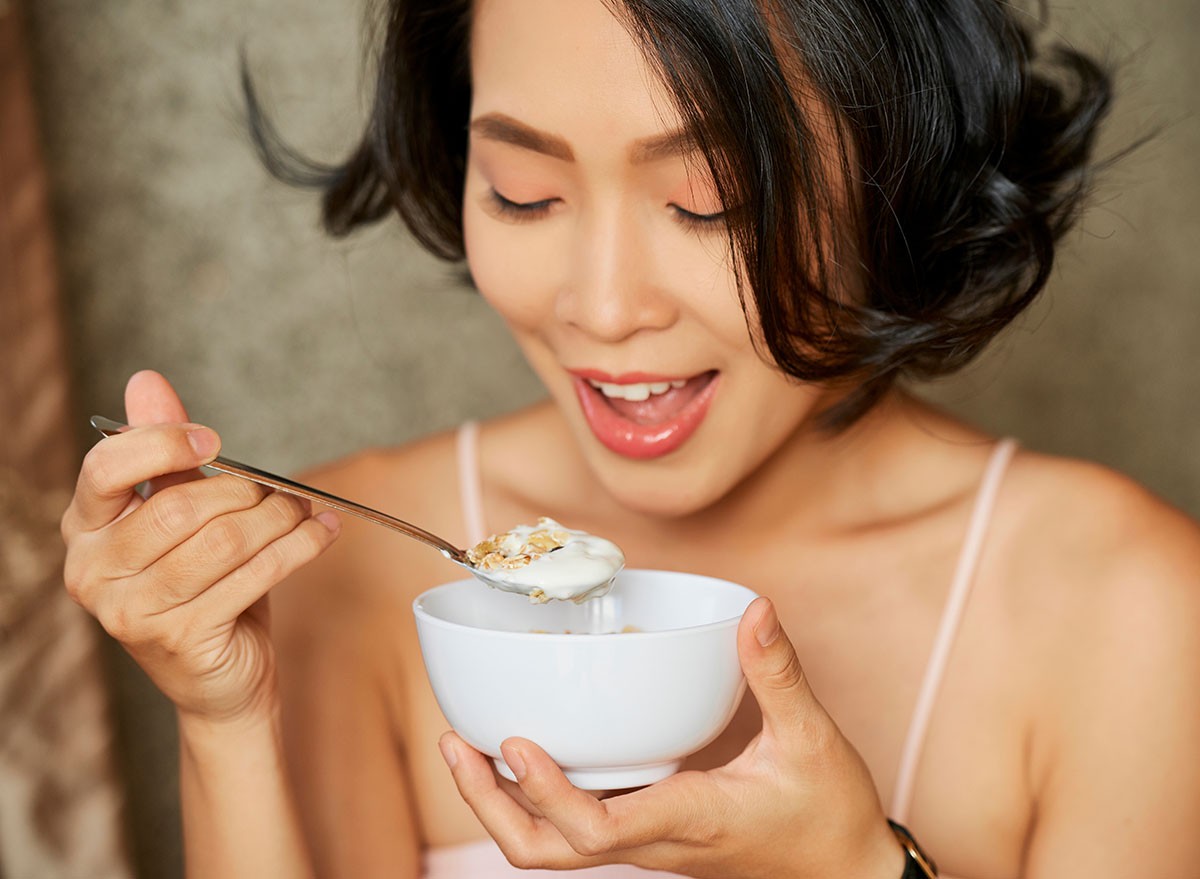 Happy young woman enjoying delicious granola with greek yogurt for breakfast