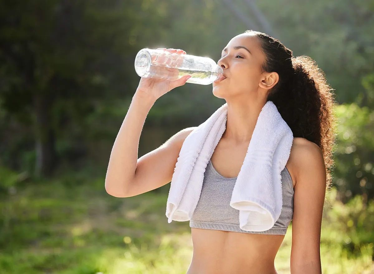 Park, bottle and drink water for girl with towel, outdoor and exercise for fitness, forest and break in nature. Wellness, healthy and woman in woods, hydration and workout with liquid and athlete