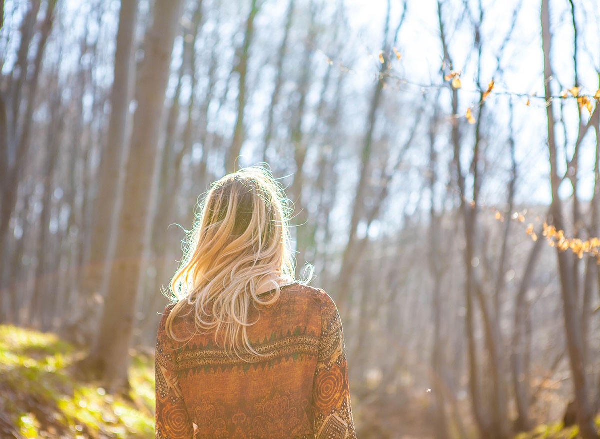 Blonde girl in the forest. Young Woman standing alone outdoor with wild forest mountains on background Travel Lifestyle. Concept view. Girl Silhouette in the forest