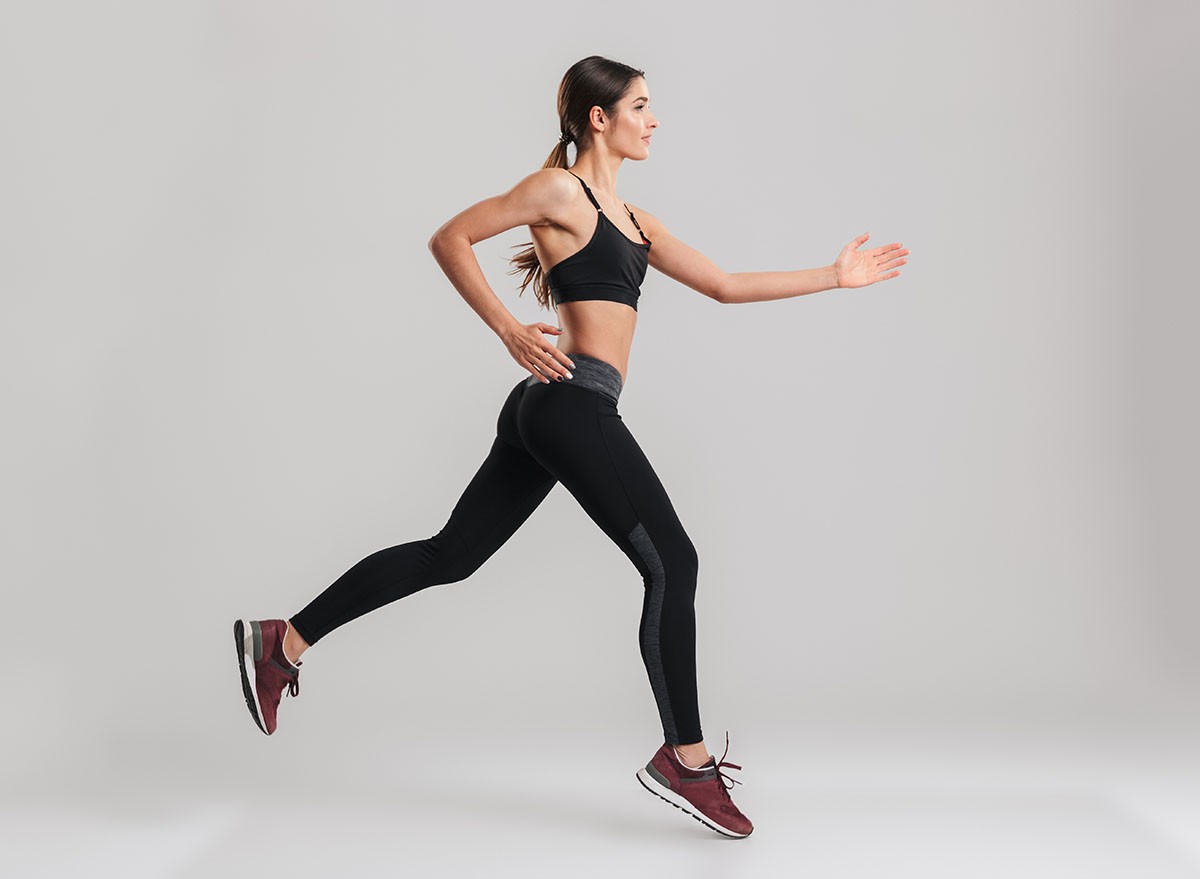 Profile picture of energetic caucasian female in sportswear running isolated along gray background