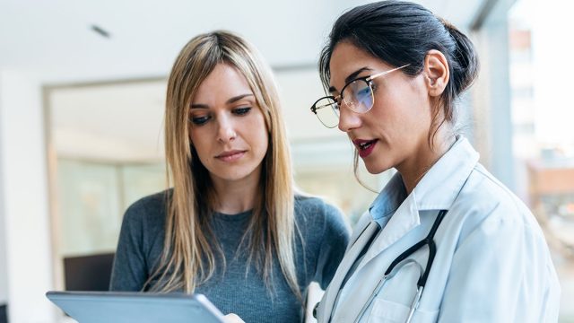 Shot of beautiful female doctor talking while explaining medical treatment with digital tablet to patient in the consultation.